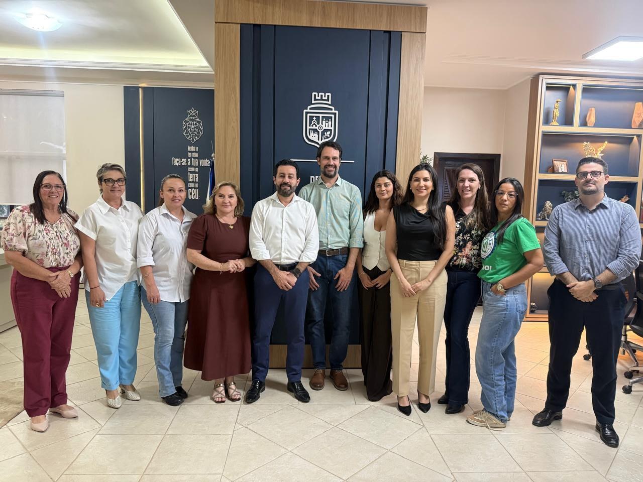 Equipe do Instituto PCI e representantes da prefeitura de Nova Mutum reunidos em frente a painel com o brasão do município